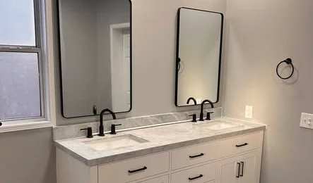 Remodeled bathroom with a white double vanity, marble-look countertop, matte black faucets and black-framed mirrors