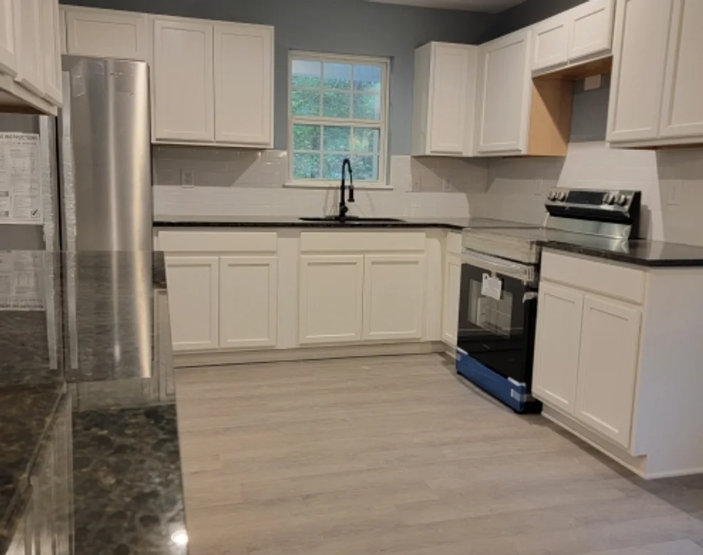 Remodeled kitchen with white shaker cabinets, dark granite countertops, stainless appliances and wide-plank vinyl flooring
