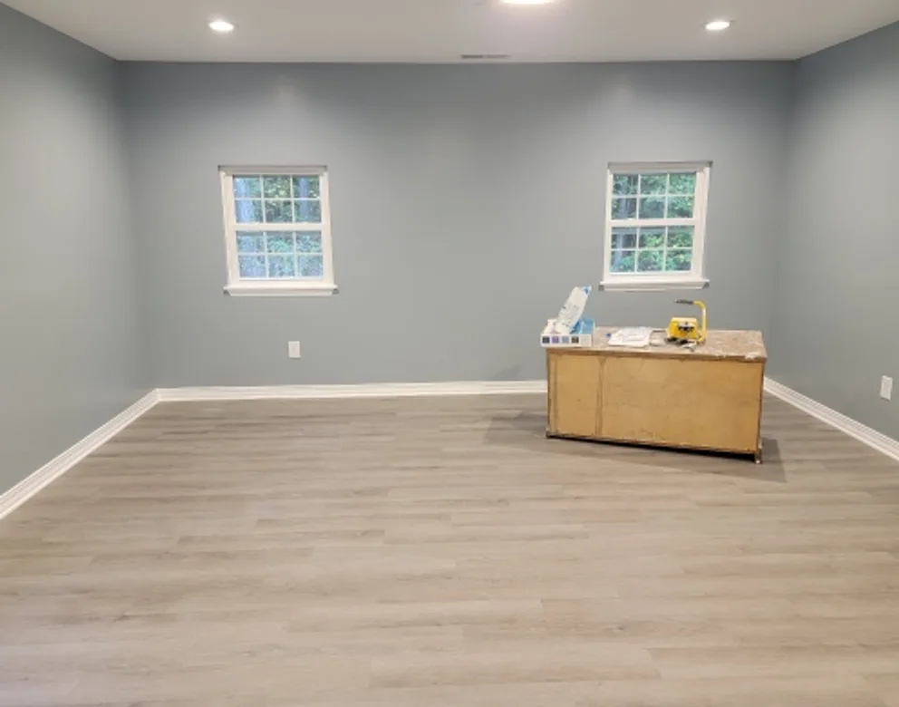 Finished room addition with gray-blue walls, two windows, recessed lighting and wide-plank vinyl flooring
